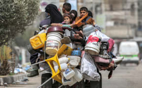 A man, woman, and children ride in the back of a tricycle loaded with belongings and other items as they flee bound for Khan Yunis, in Rafah in the southern Gaza Strip on 11 May, 2024.