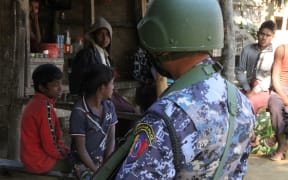 A Myanmar border guard policeman stands near a group of Rohingya Muslims at a small store in a village during a government-organized visit for journalists in Buthidaung townships in the restive Rakhine state on January 25, 2019.