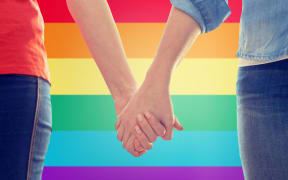 people, homosexuality, same-sex marriage, gay and love concept - close up of happy lesbian couple holding hands over rainbow flag background