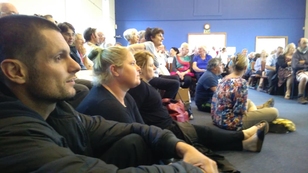 Paul Chronis and Charlotte Boocock sit on the church hall floor at a packed Island Bay meeting.