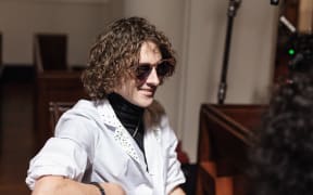 Ari Kerssens is smiling, seated at a piano in a church hall.