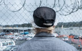 A prisoner looks out past a security fence at Paremoremo.
