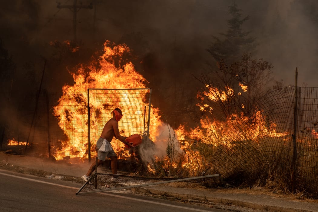 A volunteer tries to put out the fire by throwing dirt on it. A massive force of firefighters from Greece and other European countries are fighting for days.