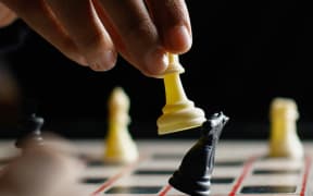 A close-up of a hand knocking down one chess piece with another.