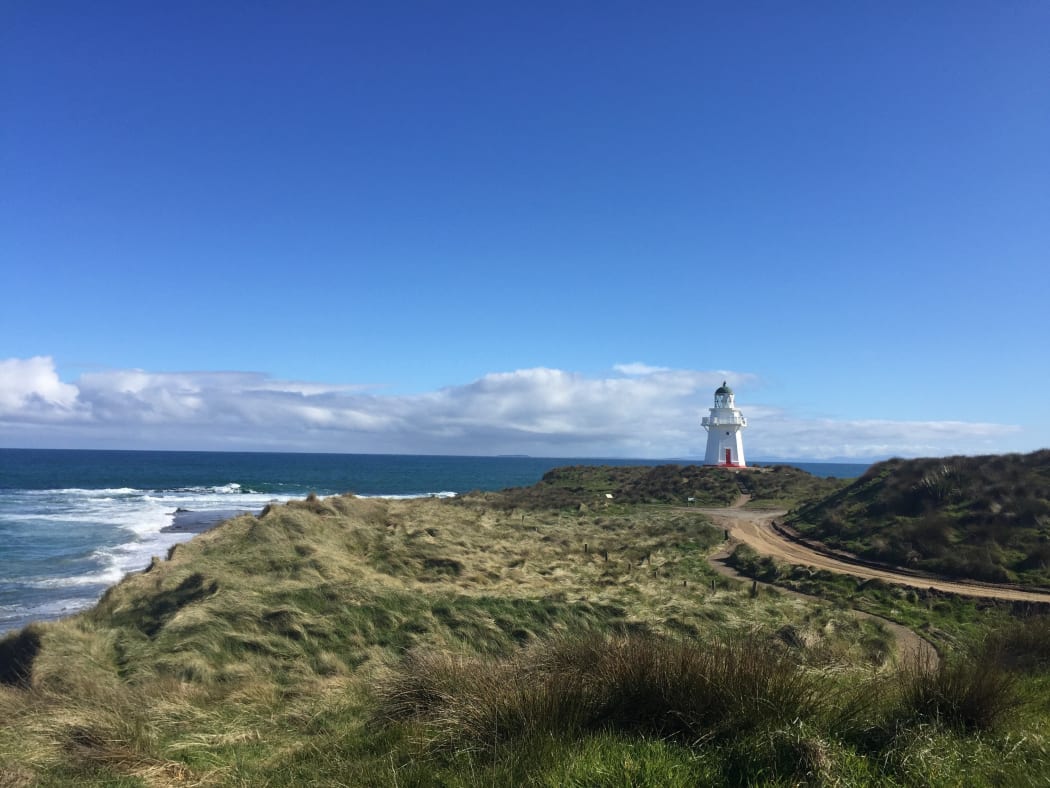 While lighthouse on coast edge with grassy stretch and path in front.