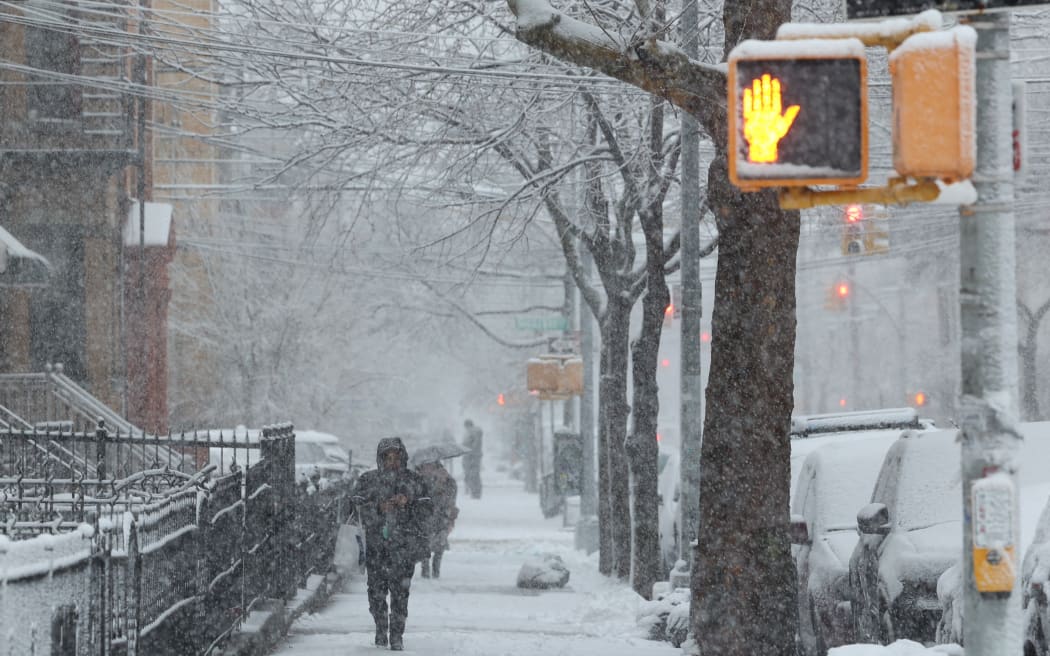 People walk on the sidewalk as snow falls in the Brooklyn borough of New York City on February 13, 2024. Heavy snowfall is expected over parts of the Northeast US starting late February 12, with some areas getting up to two inches (5cms) of snow an hour, the National Weather Service forecasters said. (Photo by Yuki IWAMURA / AFP)