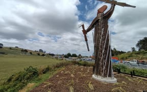 The warrior pou stands at the corner of State Highway 1 and the road to Ruapekapeka, between Hukerenui and Towai. The interpretation panel and canon are on the site of the British camp at Ruapekapeka. The canon points directly at the pa on the skyline.