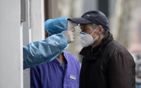 An elderly man wearing a face mask has his temperature checked before entering a community hospital in Shanghai on 13 February 2020.