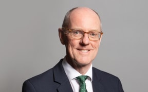 Nick smiles at the camera. he wears a suit and a green spotted tie.
