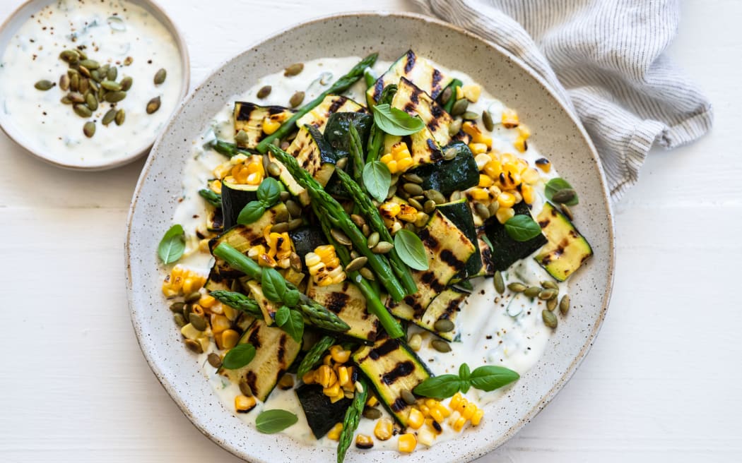 A round platter containing arbecued courgette and sweetcorn salad with basil yoghurt dressing, garnished with pumpkin seeds.
