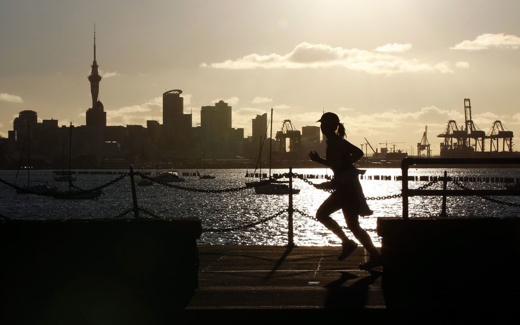A jogger runs along the seawall in Auckland with the city skyline in the background.