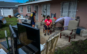 A woman sits outside her home in Tampa, Florida, as people remove debris and clean their homes after flooding caused by Hurricane Milton on 11 October 2024.