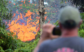 A man watches as lava is seen spewing from a fissure in the Leilani Estates subdivision near the town of Pahoa on Hawaii's Big Island on May 4, 2018. / AFP PHOTO / Frederic J. BROWN