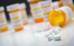 Variety of medicine bottles behind pills spilling from fallen bottle.