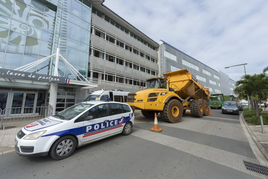 truck is parked behind a police vehicle outside the local government building as part of a protest in Noumea organised by ContraKmine, the union of mining contractors, calling on local authorities to overturn a decision on nickel exports to China on August 5, 2015.
