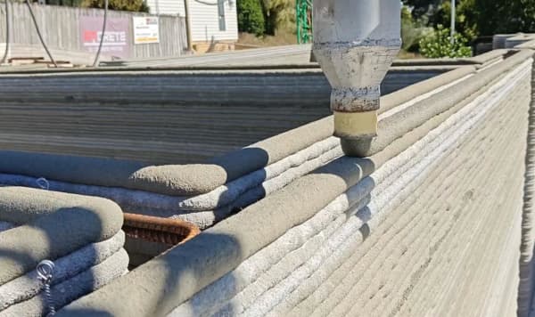 A nozzle pours multiple layers od concrete to construct the walls of a house.