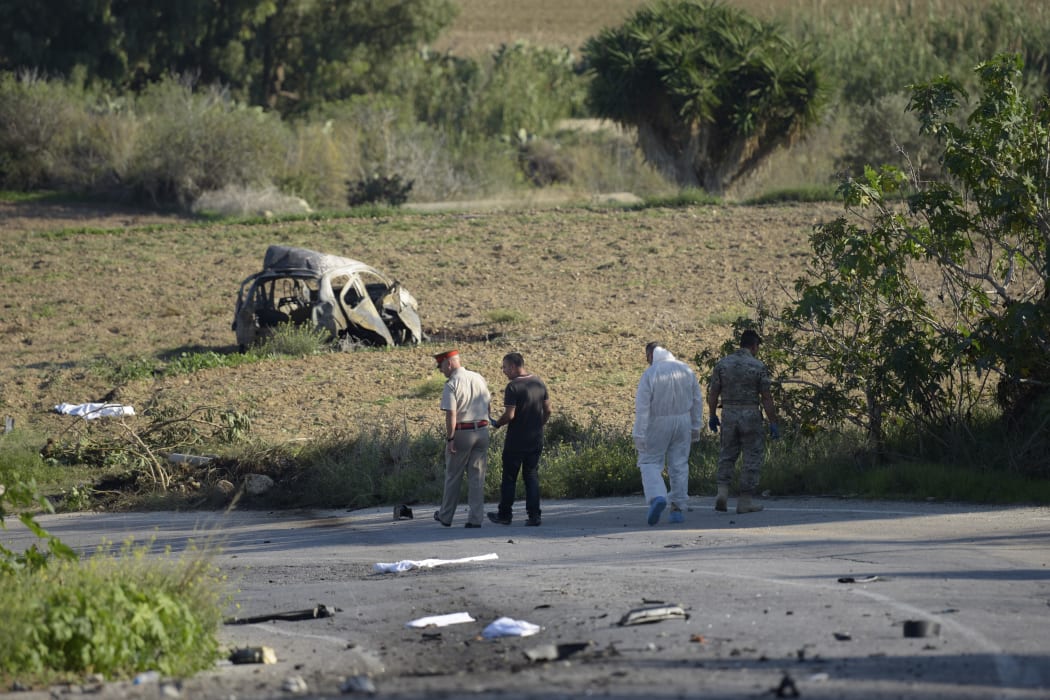 Police and forensic experts inspect the wreckage of Daphne Caruana Galizia's car.