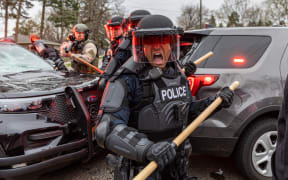 Police officers take cover as they clash with protesters after an officer shot and killed a man in Brooklyn Center, Minneapolis, Minnesota on April 11, 2021.