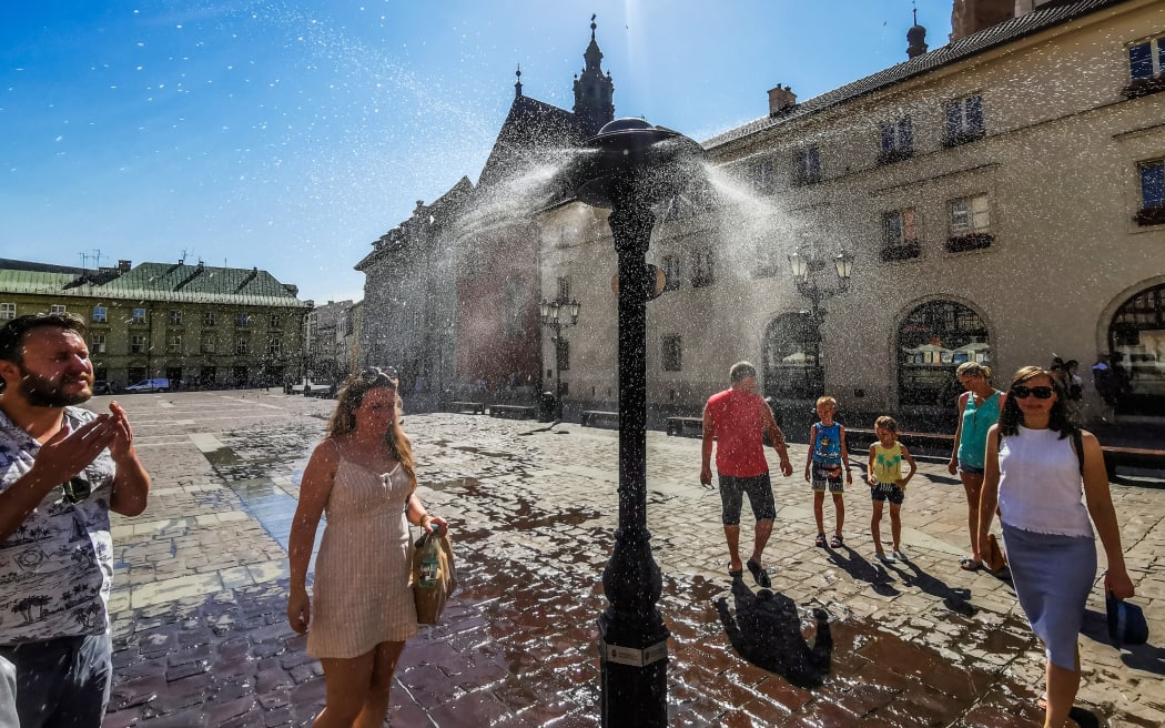 People by a water sprinkler at the Small Square in Krakow, Poland in June 2022.