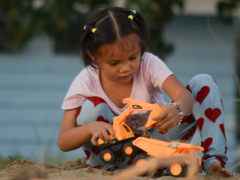 A young girl plays with a large toy truck in a sandpit.