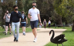 People walk past a swan around Melbourne's Albert Park Lake, 12 October 2020.