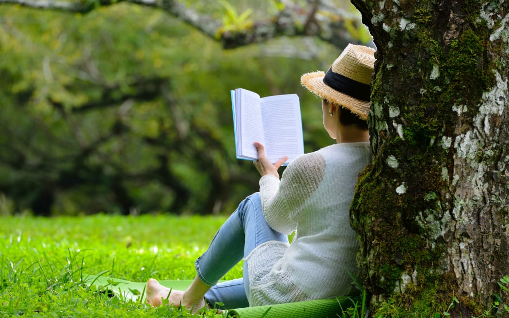 Woman sitting under a tree reading a book in the park