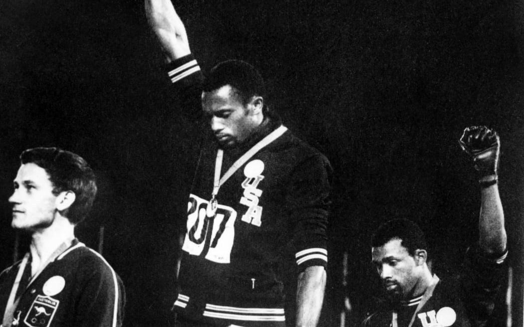 US athletes Tommie Smith (C) and John Carlos (R) raise their gloved fists in the Black Power salute to express their opposition to racism in the USA during the US national anthem, after receiving their medals 16 October 1968 for first and third place in the men's 200m event at the Mexico Olympic Games. At left is Peter Norman of Australia who took second place. (Photo by EPU / AFP)