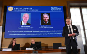 A screen shows the laureates of the 2024 Nobel Prize in Physics, US physicist John J Hopfield and Canadian-British computer scientist and cognitive psychologist Geoffrey E Hinton as member of the Nobel Committee for Physics Anders Irbaeck (R) delivers a speech following the announcement at the Royal Swedish Academy of Sciences in Stockholm, Sweden on October 8, 2024. - American John Hopfield and British-Canadian Geoffrey Hinton won the Nobel Prize in Physics on October 8, 2024 for pioneering work in the development of artificial intelligence. (Photo by Jonathan NACKSTRAND / AFP)