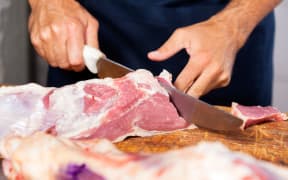 Cropped image of male butcher cutting raw meat with knife at counter in shop