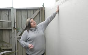 Business owner, Jennifer Rush, examines the patched-up cracks in her shop's exterior walls.