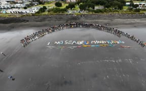 Surfboards and water craft spelled-out ‘no seabed mining’ on the black sand of Autere.