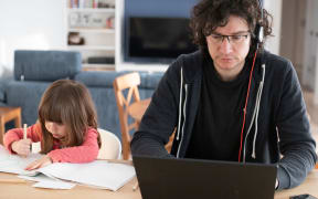 Young father working from home with little daughter drawing during covid-19 lockdown. Child drawing next to dad who is smartworking with laptop and headphones for social isolation. Front view.