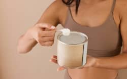 A person lifting up a scoop of supplement powder from a tin.