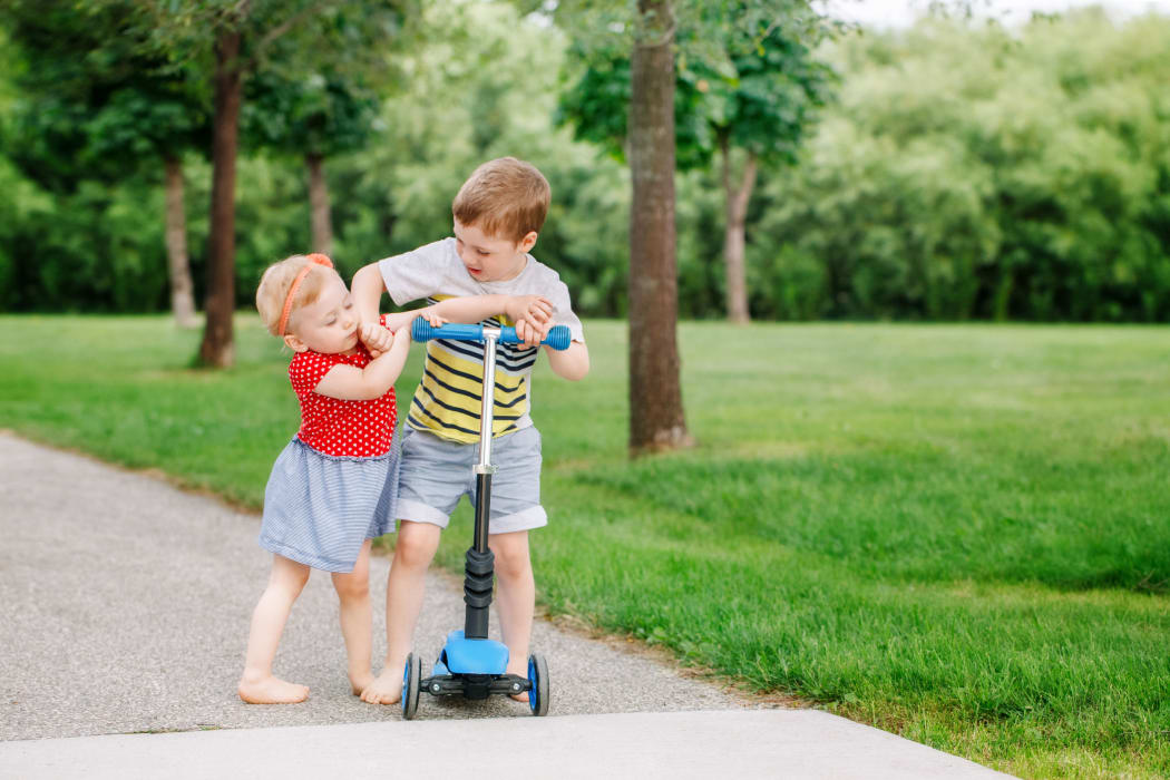 A photo of two little Caucasian preschool children fighting hitting each other. Boy and girl can not share one scooter. Older sibling brother not giving his toy to younger sister. Communication problems.