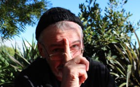 Headshot of Peter Ellis wearing a beanie with his finger held over his face, pointing skywards.