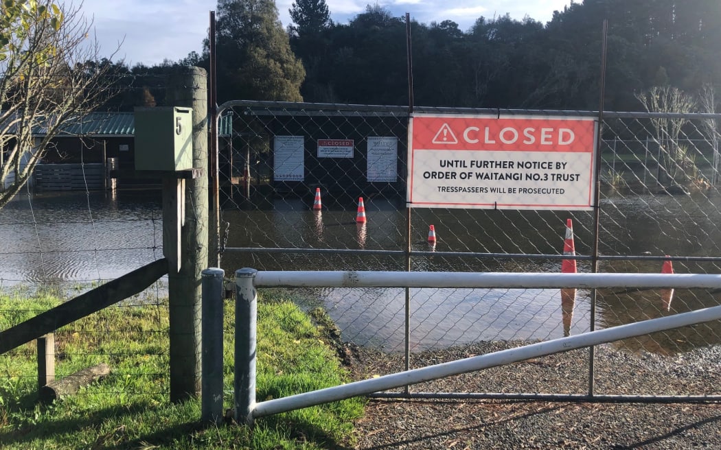 A gate with a large 'closed until further notice' sign. Behind the gate, there is flooding form the nearby lake.