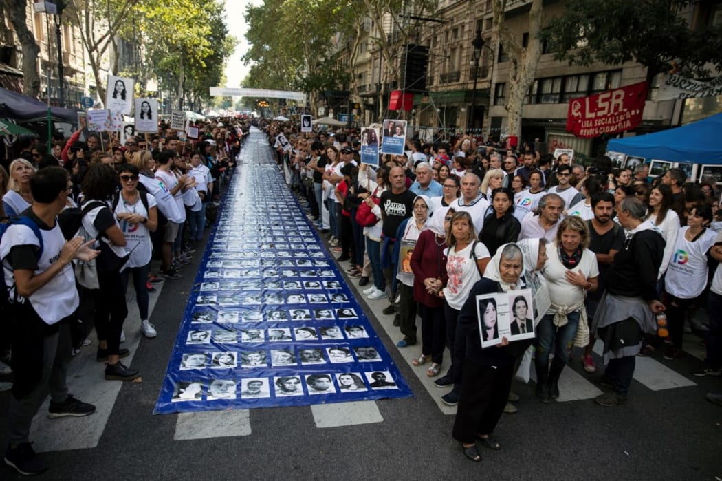 Members of the Madres de Plaza de Mayo Human Rights organization stand next to a large banner with portraits of people disappeared in the 1976-1983 military dictatorship.