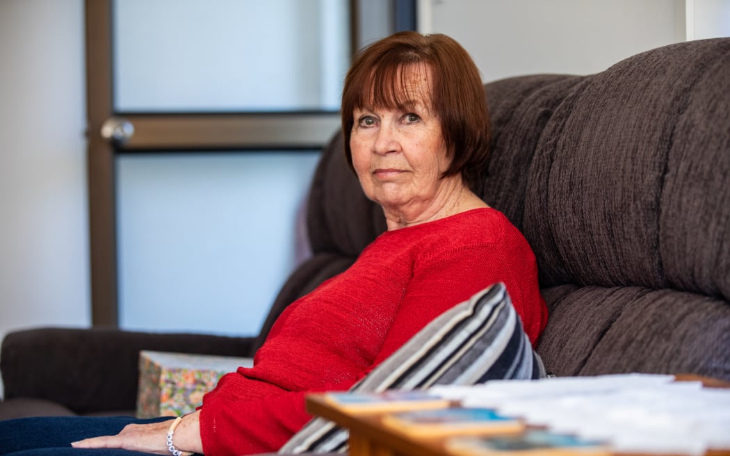 Image of a woman (Julie Appelgren) wearing a red long sleeved shirt sitting on couch, looking at the camera.