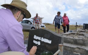 A volunteer repaints an engraved headstone with crumbling graves in the background