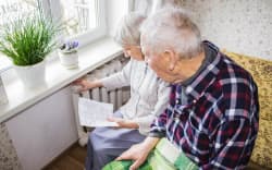 The senior woman holding gas bill in front of heating radiator. Payment for heating in winter.
