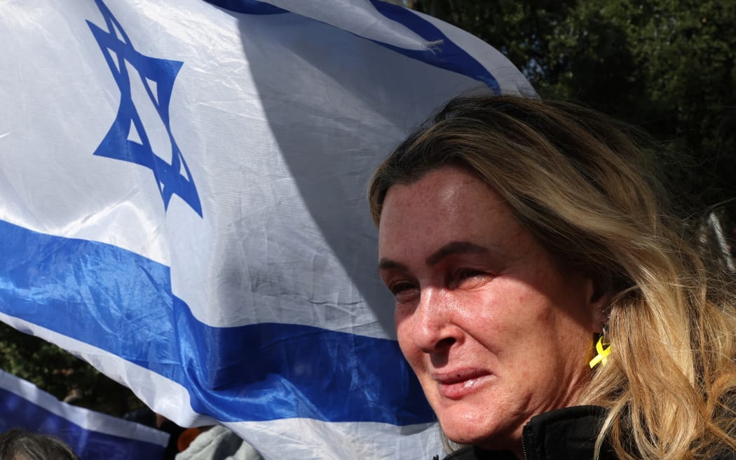 An Israeli cries as she waves the national flag upon the arrival of the convoy of vehicles transporting the bodies of the four Israeli hostages handed over by Hamas, at the National Center of Forensic Medicine in Tel Aviv on February 20, 2025. Hamas handed over the bodies of four hostages on February 20, including those of the Bibas family, who have become symbols of the hostage crisis that has gripped Israel since the Gaza war broke out. The transfer of the bodies is the first such handover of remains by Hamas since its October 7, 2023 attack on Israel triggered the war. (Photo by Jack GUEZ / AFP)