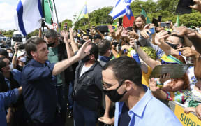 Brazil's President Jair Bolsonaro greets supporters upon arrival at Planalto Palace in Brasilia, on May 24, 2020. Despite positive signs elsewhere, the disease continued its surge in large parts of South America.