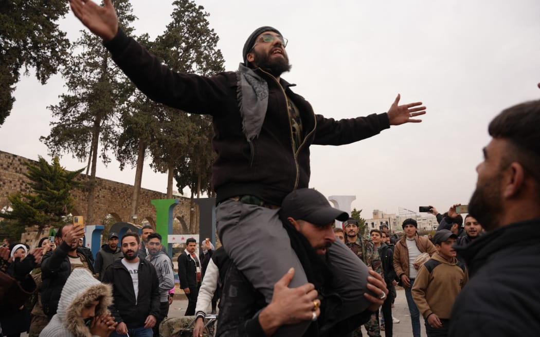 Celebrations in the city of Hama, where Syrians gather at Al-Assi Square to take commemorative photos and express their joy over the city's control. The square is filled with the sounds of celebratory gunfire and the distribution of sweets to mark the occasion.