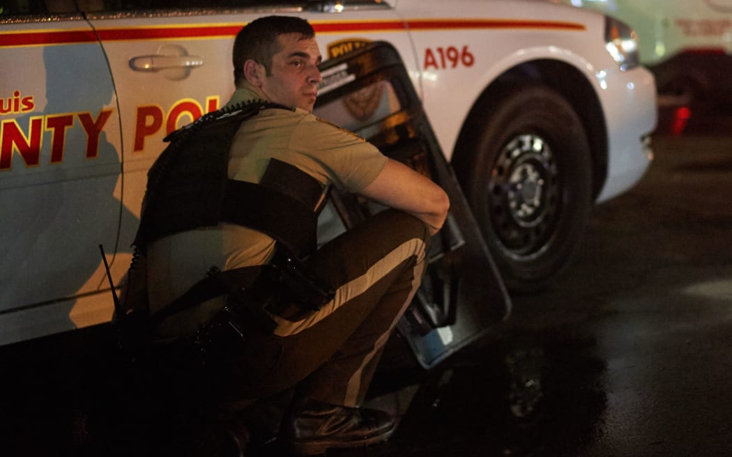 A St Louis County police officer takes cover behind a car after shots were fired during a protest march in Ferguson, Missouri.