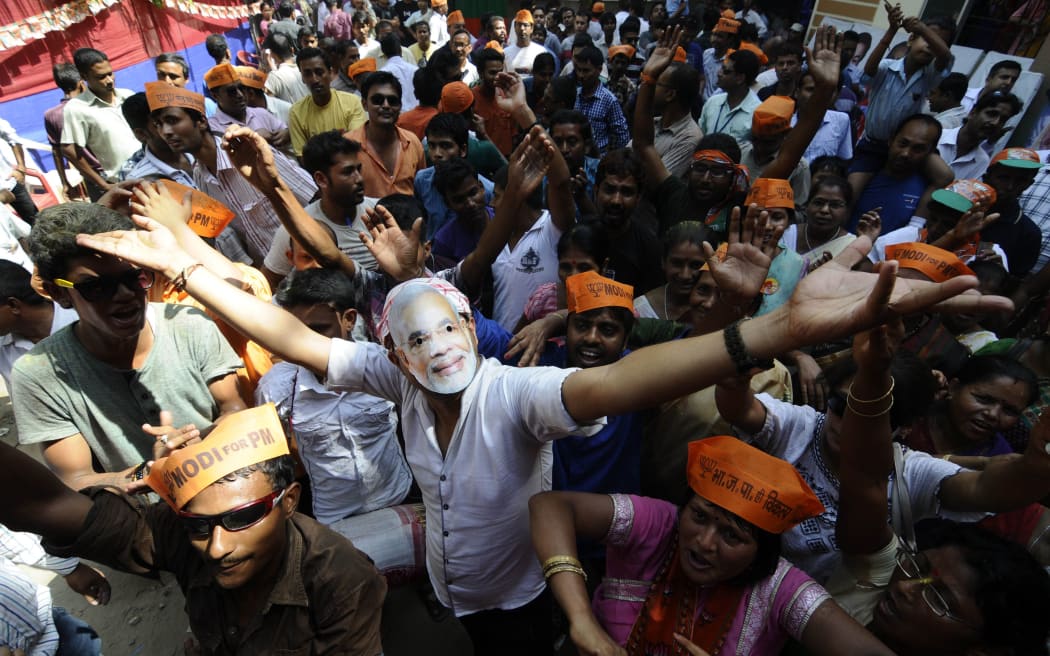 BJP workers, one wearing a mask of Narendra Modi, celebrate outside the party office in Guwahati.