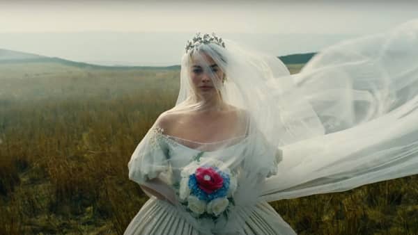Margot Robbie wears a wedding gown and veil and stands in a field.