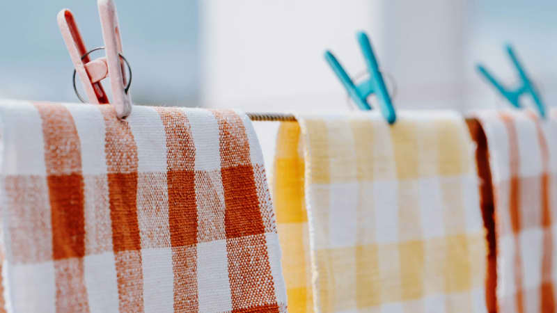Checkered kitchen towels hanging to dry on a clothesline outdoors.