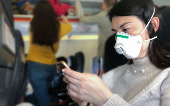 Airplane passenger with with respiratory mask looking at phone.