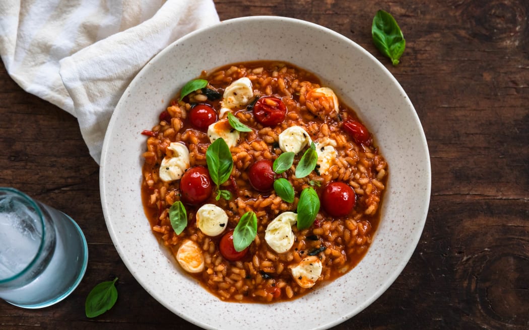 A bowl of Cherry tomato and mozzarella risotto decorated with basil leaves