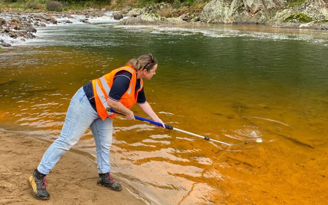 Council staff collecting samples of the river that has been contaminated by an orange substance.